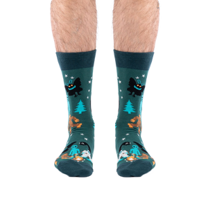 Front view of a person's lower legs, showing both dark green cryptid socks featuring Bigfoot and Mothman.