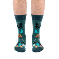 Front view of a person's lower legs, showing both dark green cryptid socks featuring Bigfoot and Mothman.