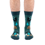 Front view of a person's lower legs, showing both dark green cryptid socks featuring Bigfoot and Mothman.