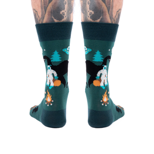 Back view of a person's lower legs with tattoos, wearing dark green cryptid socks with Yeti, Mothman, and UFO.
