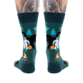 Back view of a person's lower legs with tattoos, wearing dark green cryptid socks with Yeti, Mothman, and UFO.