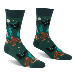 Pair of dark green crew socks with a repeating pattern of Bigfoot, Mothman, alien, Yeti, campfire, trees, moon, and stars.