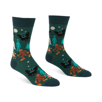 Pair of dark green crew socks with a repeating pattern of Bigfoot, Mothman, alien, Yeti, campfire, trees, moon, and stars.