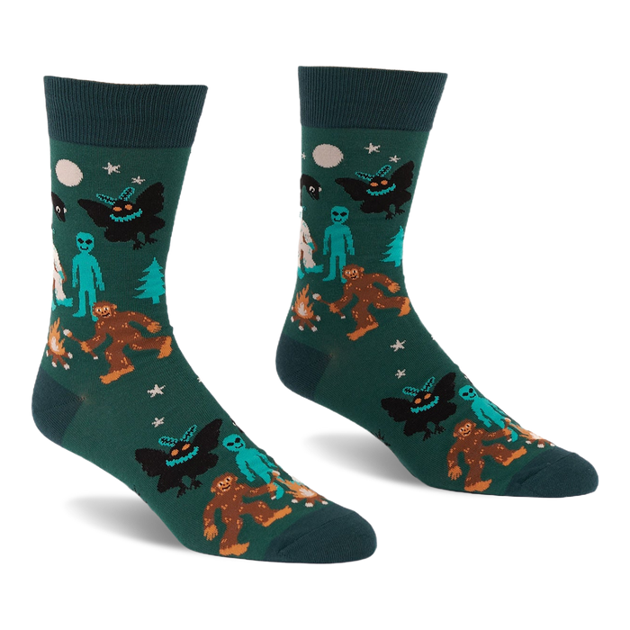 Pair of dark green crew socks with a repeating pattern of Bigfoot, Mothman, alien, Yeti, campfire, trees, moon, and stars.