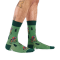 Person's lower legs and feet, seen from the side, wearing green raccoon bicycle socks. White background.