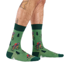 Person's lower legs and feet, seen from the side, wearing green raccoon bicycle socks. White background.