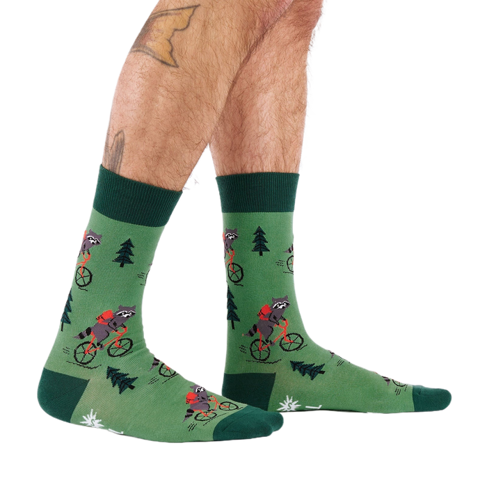 Person's lower legs and feet, seen from the side, wearing green raccoon bicycle socks. White background.