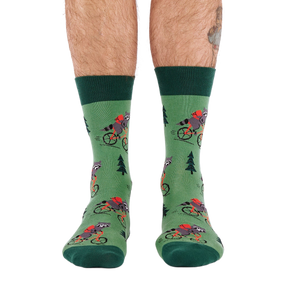 Person's lower legs and feet, seen from the front, wearing green raccoon bicycle socks. White background.