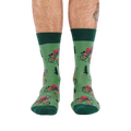 Person's lower legs and feet, seen from the front, wearing green raccoon bicycle socks. White background.