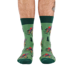 Person's lower legs and feet, seen from the front, wearing green raccoon bicycle socks. White background.
