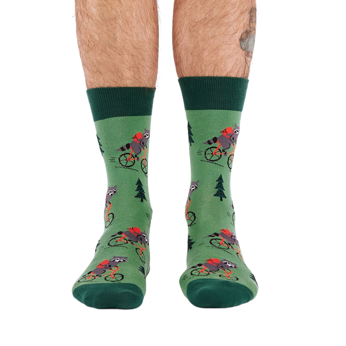 Person's lower legs and feet, seen from the front, wearing green raccoon bicycle socks. White background.