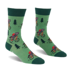 Pair of green socks with raccoons on red bicycles, wearing red backpacks, among dark green pine trees. Darker green cuffs, heels, toes.