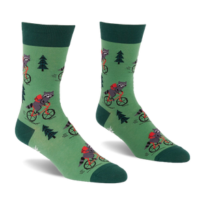 Pair of green socks with raccoons on red bicycles, wearing red backpacks, among dark green pine trees. Darker green cuffs, heels, toes.