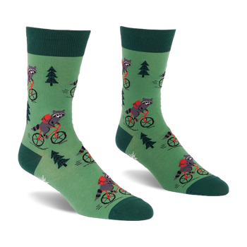 Pair of green socks with raccoons on red bicycles, wearing red backpacks, among dark green pine trees. Darker green cuffs, heels, toes.