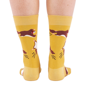 Person standing, wearing mustard yellow crew socks with flying squirrel pattern, viewed from the back.