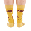 Person standing, wearing mustard yellow crew socks with flying squirrel pattern, viewed from the back.