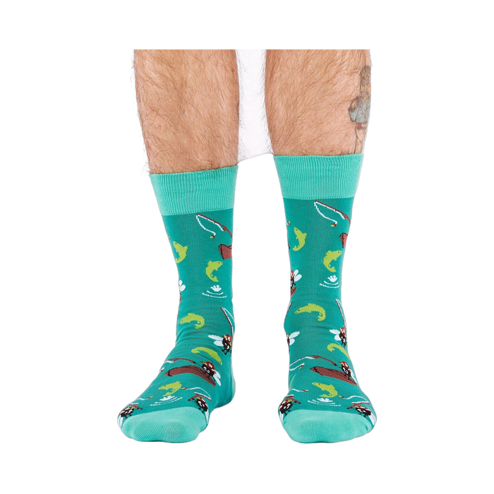 Front view of a person wearing teal fly fishing socks, showing leg hair and a partial tattoo on the right calf.