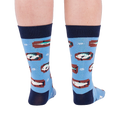 Person standing backward, showing the heels of light blue crew socks with fish and knot patterns on a white background.