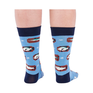 Person standing backward, showing the heels of light blue crew socks with fish and knot patterns on a white background.