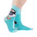 Person wearing light blue socks showing a large puffin on the ankle with an orange beak and white starbursts near the sole.