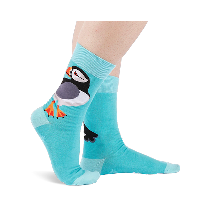 Person wearing light blue socks showing a large puffin on the ankle with an orange beak and white starbursts near the sole.