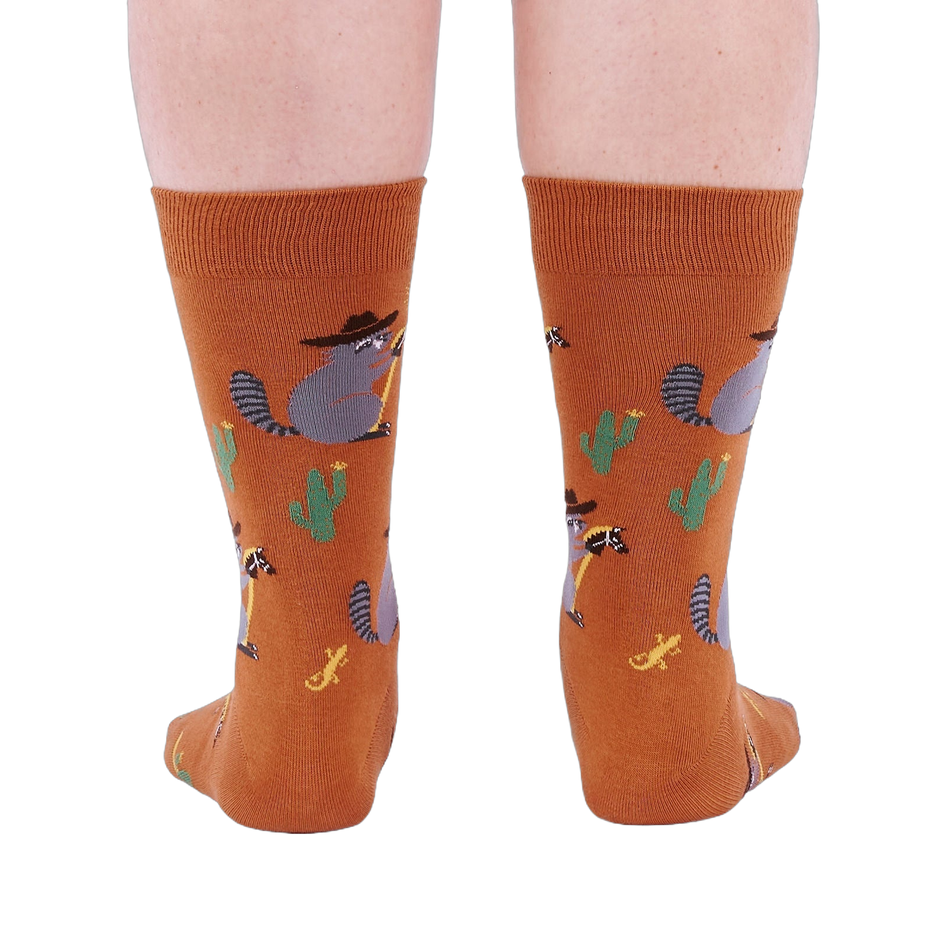 Back view of a person wearing burnt orange crew socks with a repeating pattern of raccoon cowboys, cacti, suns, and lizards.