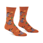 A pair of burnt orange crew socks with cartoon raccoons in cowboy hats lassoing, green cacti, yellow suns, and lizards.
