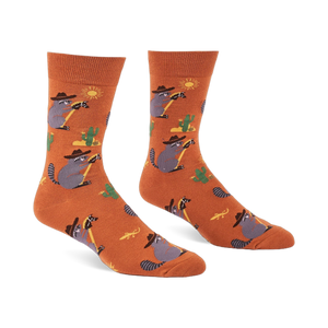 A pair of burnt orange crew socks with cartoon raccoons in cowboy hats lassoing, green cacti, yellow suns, and lizards.