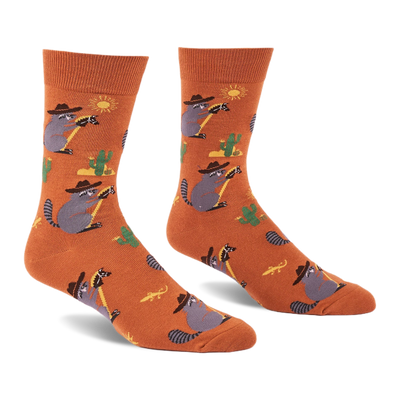 A pair of burnt orange crew socks with cartoon raccoons in cowboy hats lassoing, green cacti, yellow suns, and lizards.