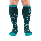Front view of legs wearing dark teal knee-high socks with turquoise cuffs, showing scattered masks, roses, and musical notes.