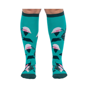 Front view of a person's legs wearing teal knee-high socks with pink and dark green philodendron leaves.