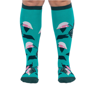 Front view of a person's legs wearing teal knee-high socks with pink and dark green philodendron leaves.