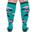 Back view of a person's legs wearing teal knee-high socks with pink and dark green philodendron leaves.