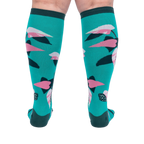 Back view of a person's legs wearing teal knee-high socks with pink and dark green philodendron leaves.