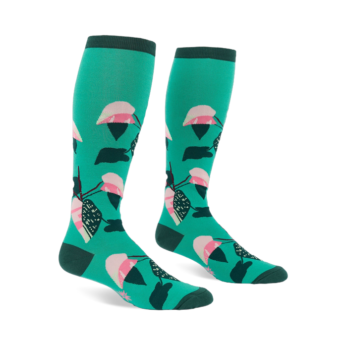 Pair of knee-high teal socks with a repeating philodendron leaf pattern in pink, white, dark green, and black. Dark green cuffs, heels, and toes.