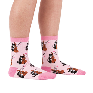 A person's lower legs wearing the light pink musical cat crew socks, shown from the side against a white background.