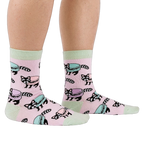 Side view of a person wearing pink crew socks with a pattern of raccoons and pastel macarons, showing light green cuffs and heels.