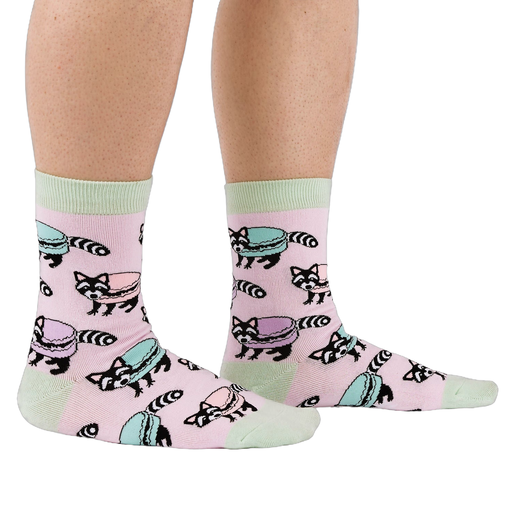 Side view of a person wearing pink crew socks with a pattern of raccoons and pastel macarons, showing light green cuffs and heels.