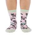 Front view of a person wearing pink crew socks adorned with a pattern of cartoon raccoons and light blue and purple macarons.