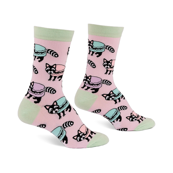 Pair of pink crew socks with light green accents, featuring a repeating pattern of cartoon raccoons and pastel macarons.