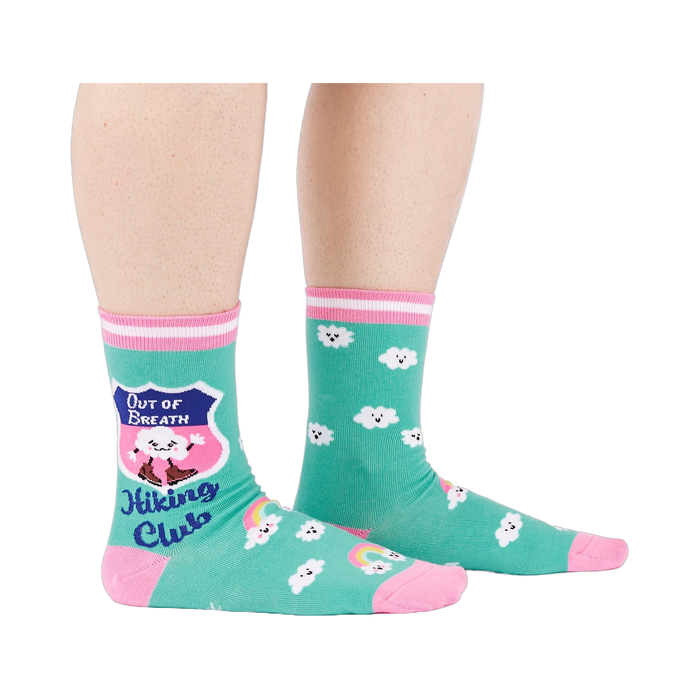 A person's legs wearing teal 'Hiking Club' crew socks, posed on a white background. Left sock shows shield design.