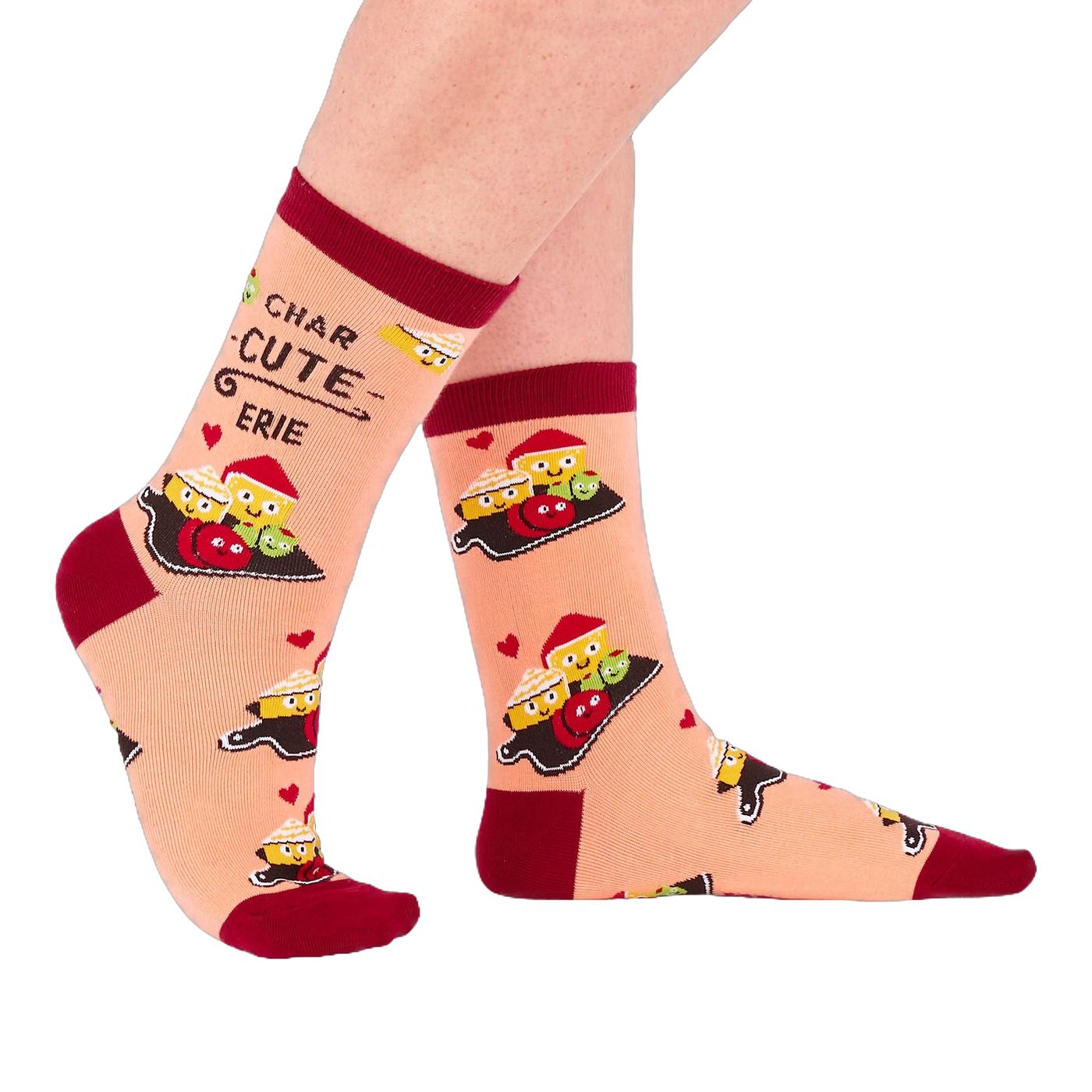 Person wearing peach "Char-cute-erie" socks, shown from the side. Socks feature smiling food characters, red hearts, and text on a light background with dark red accents.