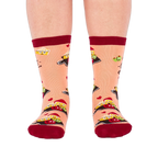 Person wearing peach "Char-cute-erie" socks, shown from the front. Socks display smiling food characters on dark boards, red hearts, and dark red cuffs, heels, and toes.