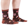 Person standing on a white floor, wearing brown crew socks patterned with cupcakes, pretzels, and chocolate.