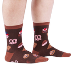 Person standing on a white floor, wearing brown crew socks patterned with cupcakes, pretzels, and chocolate.