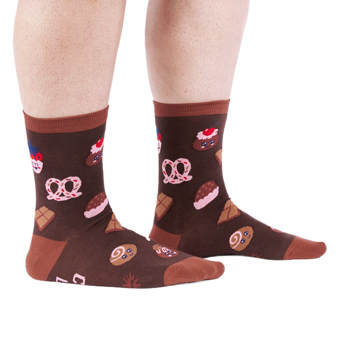Person standing on a white floor, wearing brown crew socks patterned with cupcakes, pretzels, and chocolate.