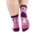 Person wearing 'Snuggle Bunny' socks, back view. Sock bottom shows 'SNUGGLE BUNNY' text and a red starburst.
