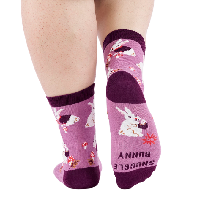 Person wearing 'Snuggle Bunny' socks, back view. Sock bottom shows 'SNUGGLE BUNNY' text and a red starburst.