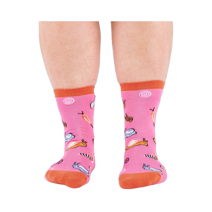 Front view of someone's lower legs wearing pink socks with colorful jelly candy snails, candy swirls, and an orange cuff.