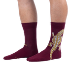 A person wearing burgundy crew socks with a large tan and yellow bearded dragon printed on the outer side of the leg.